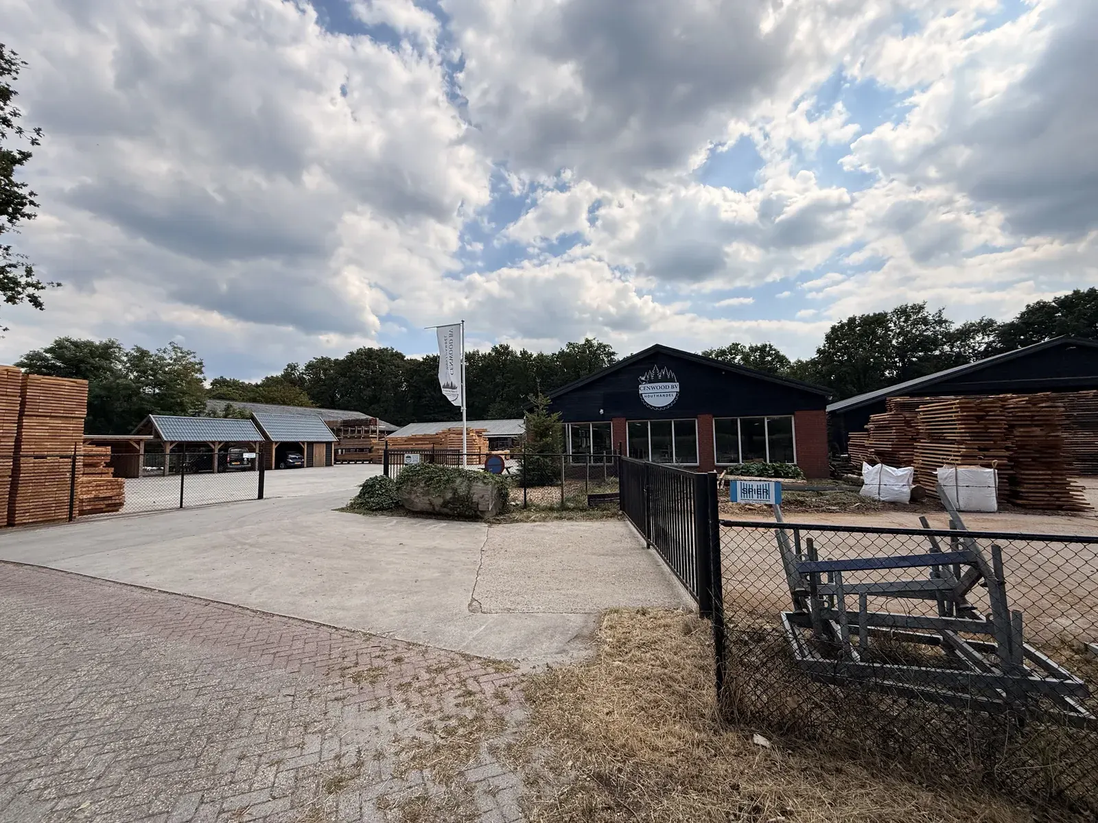 Entree met hek van houthandel CenWood in Gemert, met bedrijfspand en houtstapels erachter